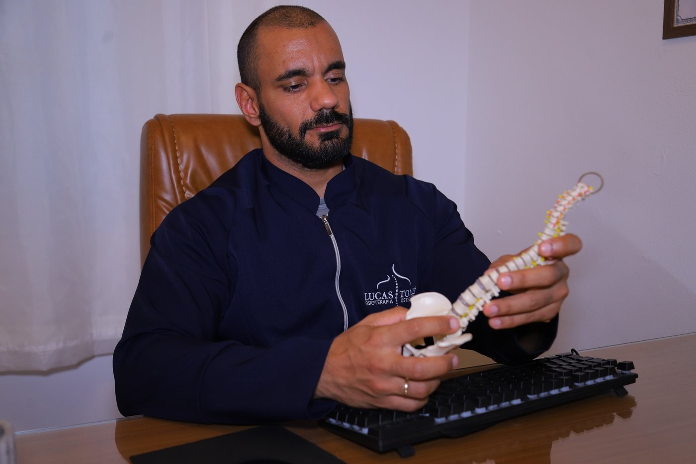 Lucas Tomé mostrando um modelo anatômico da coluna vertebral no consultório em Valinhos